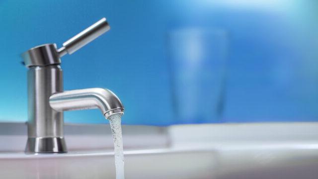 Water flows out of a faucet against a blue background, representing Tetra Tech’s drinking water services