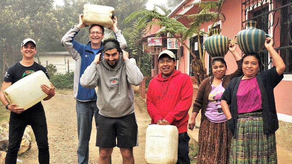 A group of people helping Mayan villagers in Guatemala carry water jugs to their homes